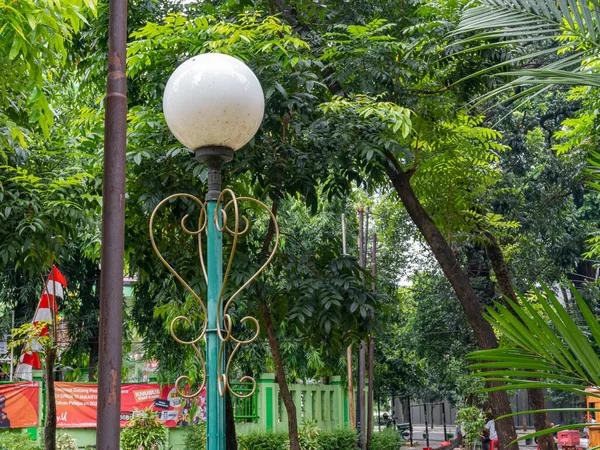 A circular white park lamp standing on top of a green pole on a sunny day.