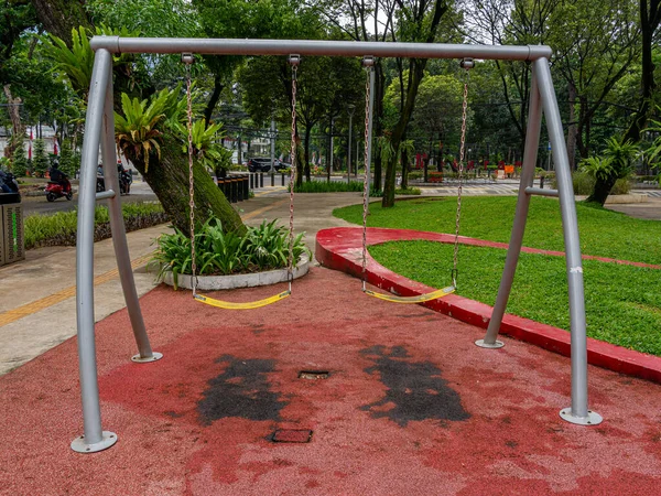 A pair of iron swings made for both children and adults on a pink bitumen floor at a public park.