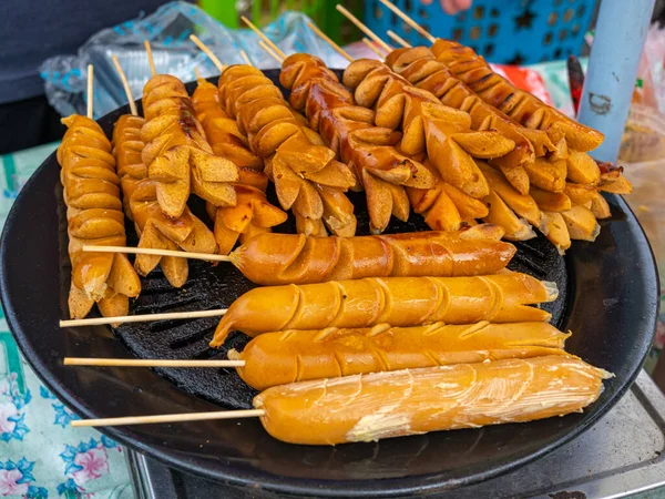 A group of sausage satay being cooked over a black hot pan during a street food bazaar