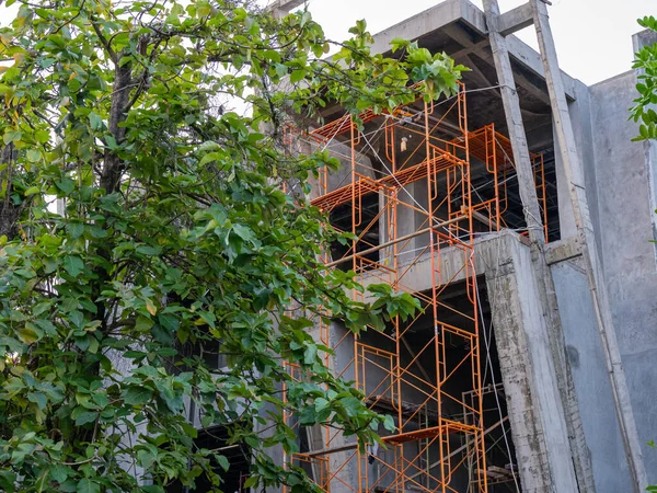 A vertical arrangement of orange scaffolding being erected to form proper footing for workers of a concrete construction.