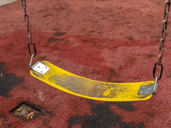 An aged yellow polymer belt swing seat with a pair of iron chains and hooks at a public park.