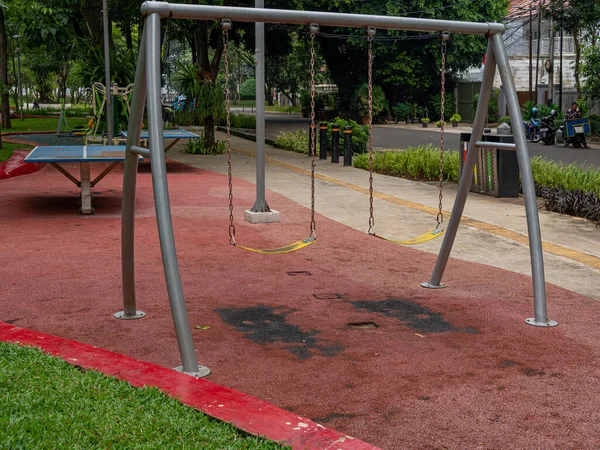 A pair of iron swings strongly placed on a red bitumen at a public park.
