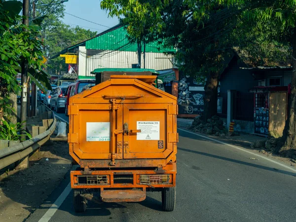 Jakarta, Indonesia - August 26, 2022: A rear view of an orange light garbage transporting vehicle waiting for traffic queue on a sunny afternoon.