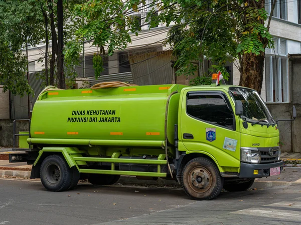 Jakarta, Indonesia - August 19, 2022: A green tanker truck is parked under a tree and ready to perform its duty on a sunny morning.
