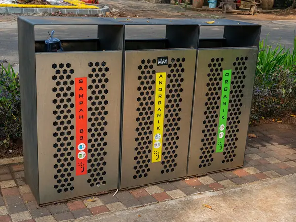 Jakarta, Indonesia - August 19, 2022: Three metal garbage bins at a city park with each colored classifications and words saying 