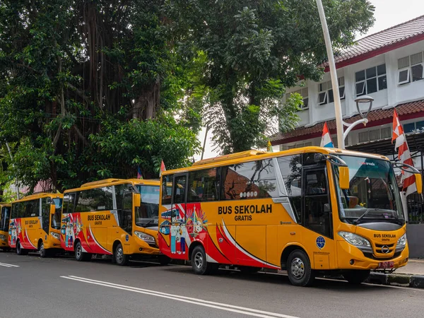 Jakarta, Indonesia - August 17, 2022: Four orange school buses are parked in line in front of a secondary school in Jakarta on a sunny morning.