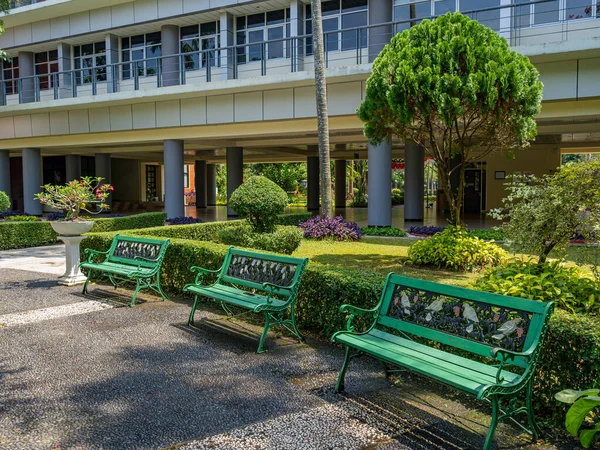 Depok, West Java, Indonesia - August 12, 2022: Three green park benches in front of the faculty administration building, the University of Indonesia.