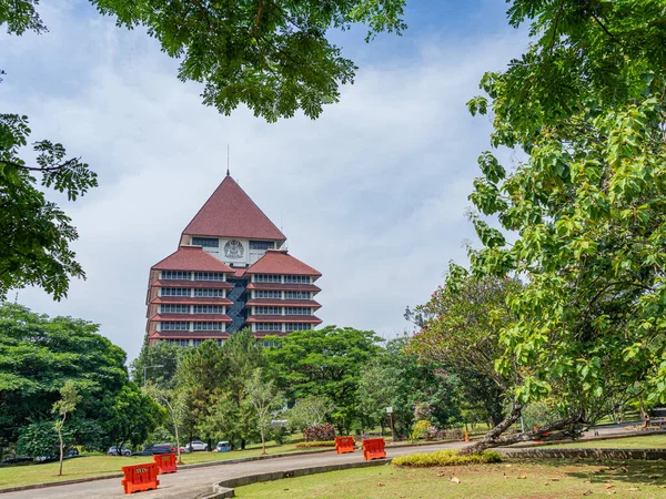 Depok, West Java, Indonesia - September 24, 2022: Large landscape view of the center for administration building of the University of Indonesia with vegetation framing and clear blue sky.