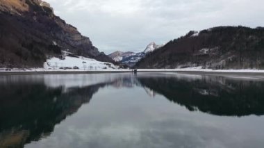 Amazing 4K aerial footage over an alpine lake surrounded by mountains, forest and snow.