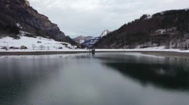 Amazing 4K aerial footage over an alpine lake surrounded by mountains, forest and snow.