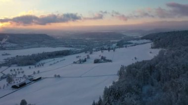 Great 4K aerial footage of a snowy forest in Switzerland in the lowlands during a beautiful sunset.