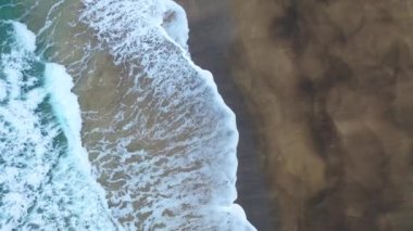 4K aerial footage of a golden sandy beach partly submerged by water and covered by snow in Iceland.