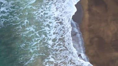 4K aerial footage of a golden sandy beach partly submerged by water and covered by snow in Iceland.