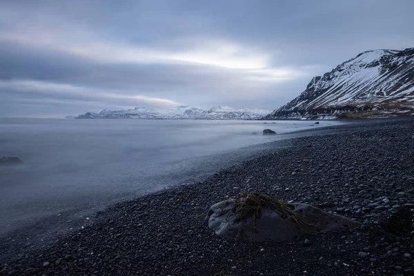 在冰岛长期暴露在一个黑色海滩上 前景是石头和海藻 背景是群山 — 图库照片