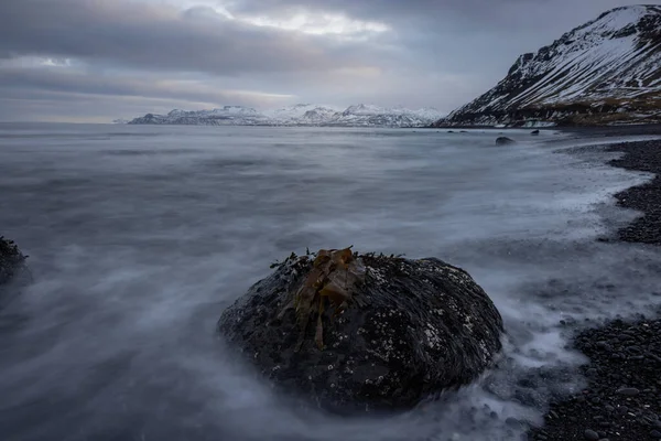 手前に石と海苔 奥に山が見える黒いビーチでのアイスランドでの長い露出 — ストック写真