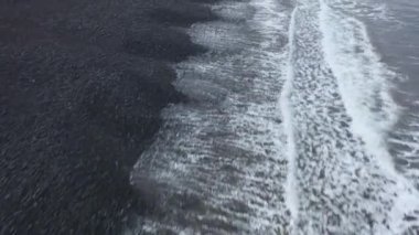 İzlanda 'da siyah bir kumsal üzerinde 4K hava görüntüsü turkuaz mavi suyun siyah volkanik kayayla buluştuğu yerde..