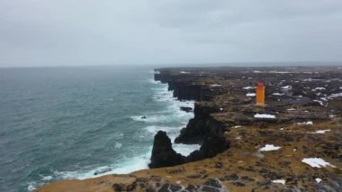 4K aerial footage of an orange lighthouse in northern Iceland on a snowy day in winter.