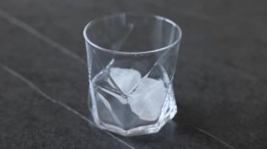 A single malt scotch whiskey is poured into a glass with ice cubes in slow motion. Whiskey on the rocks.