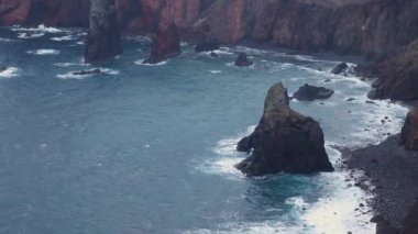 Madeira kıyısındaki yağmurlu bir günün 4K videosu dalgaların kırmızı volkanik kayalıklara çarptığı yer..
