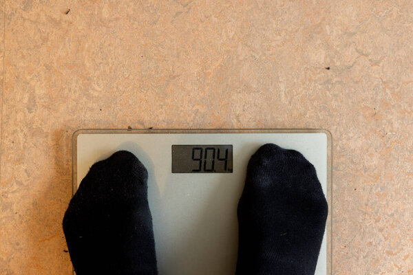 Мужчина стоит на весах и весит более 90 кг, что значительно выше среднего для мужчин.