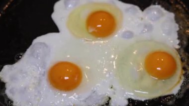 Bir şef siyah bir tavada üç yumurta kızartır ve tabakta servis eder..