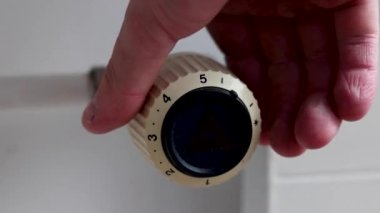 Enerji krizleri sırasında ısıtma faturalarını azaltmak için radyatörün termostatını kapatan bir adam..