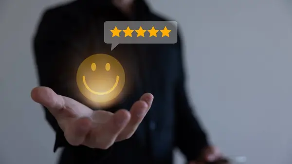 Businessman using a mobile phone to point to a smile face and five stars icon, representing positive reviews and customer satisfaction. Building credibility and trust with happy customers.