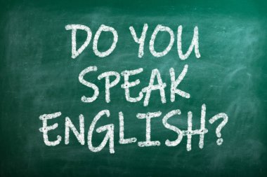 Üzerinde yazı olan bir karatahta İngilizce biliyor musun? Kalemlerle dolu bir demlik ve İngiltere bayrağı, ahşap bir masada, yeşil arka planda.