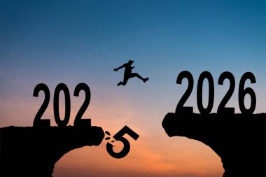 Yeni Yıl 2026, ilham ve yeni başarı yolunda ilerleme. İnsan siluetleri uçurumdan bitiş çizgisine doğru atlıyor. Yeni yıl 2026 günbatımında güzel bir yazı.