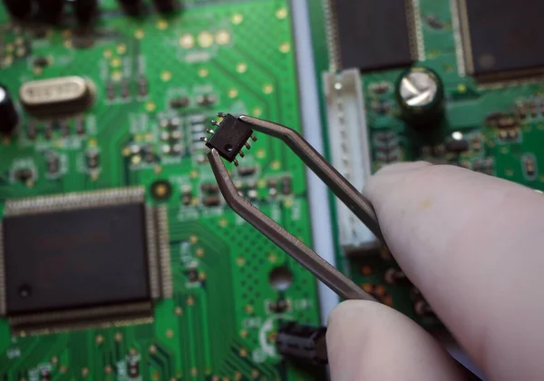 Holding a microchip on the electronic circuit board. Surface-mount technology card repair. Selected focus.