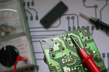 Elektronik tamir tezgahı. Çoklu sayacı, çipi ve diyagramı olan elektronik devre kartı. Kırmızı sondaya odaklanmış..