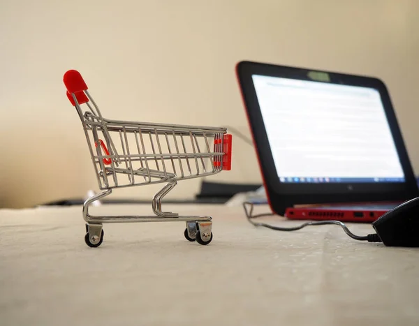 Empty shopping trolley going into the blank screen computer. Cart into the internet store. Retail trade or e-commerce.