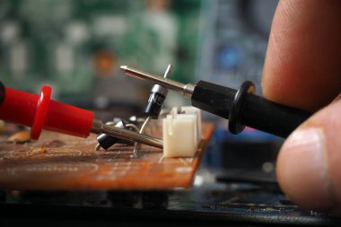Devre kartında elektronik bileşeni test eden teknisyen. Diyota odaklanmış.