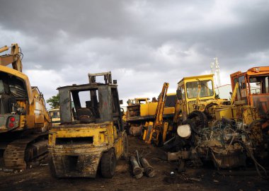Dramatik gökyüzünün altındaki hurdalıkta buldozer ve makine parçalarını çöpe at. Kullanılamaz durumda inşaat ekipmanları ve yedek parça veya geri dönüşüm için metal malzemeler. Kısmi ışık.