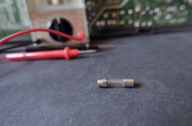 Kartuş fünyesi (cam sigorta) ohmmetre ile test etmek için tezgahın üzerinde duruyor. Sigortaya odaklanmış..