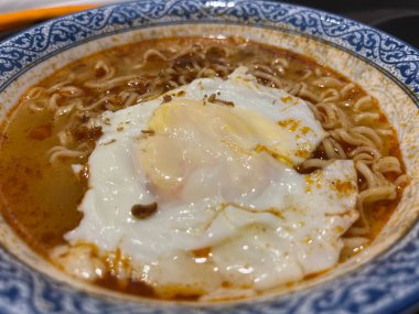 Bir kase eriştenin üstünde yumurta olan yakın plan fotoğrafı.