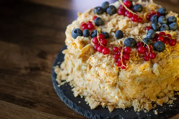 Olgun yaban mersinleri ve canlı kırmızı üzümlerle süslenmiş güzel katmanlı bir pasta, ahşap masa ambiyansıyla çevrili, koyu bir taş tepside, kutlama için mükemmel..
