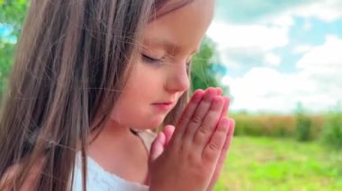 Küçük kız dua ediyor, gökyüzüne umutla bakıyor, portreyle. Şirin küçük kız ellerini doğada dua ederken kavuşturdu..