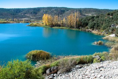 Shores of the lagoon with turquoise waters with autumn-colored trees and surrounded by green mountains.