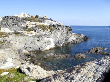 Cadaques, Girona 'daki Costa Brava' nın berrak gökyüzü ve mavi suyuyla çelişen gri kayalar..