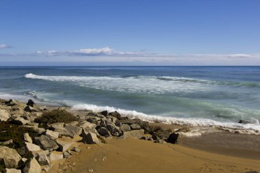 Ufukta mavi ve bulutların çeşitli tonlarında taşları ve suyu olan altın kumsal..
