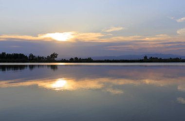 Pembe bulutların ardında gün batımı, sakin su aynasından yansıyor..