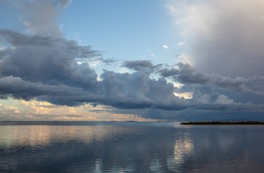Koyda oynayan ışıklar ve bulutlar melankolik bir dokunuşla sakin bir atmosfer yaratıyor..