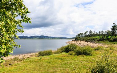 Güneşli bir günde etrafı dağlarla, ağaçlarla ve yeşil bitkilerle çevrili bir gölgelik. Galiçya, İspanya.