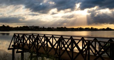 View of the sunrise between clouds over the Ebro River from the walkway in the Ebro Delta, Catalonia, Spain. clipart