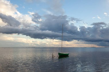 Small sailing boat under the sunset with clouds on the horizon in the Ebro Delta, Catalonia, Spain clipart