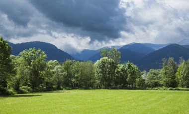 Fırtınalı bulutlarla kaplı dağlar La Cerdanya, Katalonya, İspanya 'daki yeşil güneşli çayırlarla çelişiyor.
