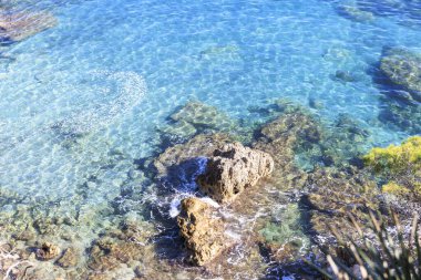 crystal-clear blue water gently lapping at the rock formations on the shore