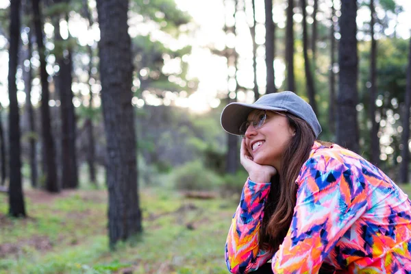 stock image latina woman with cap and multicolored sport jacket happy in the forest