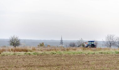 Büyük mavi bir traktör tarlayı sürmeye ve önceden kesilmiş mısırın kalıntılarını temizlemeye hazır..